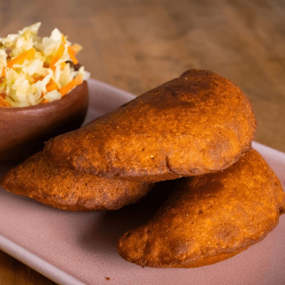 Three golden-brown Mexican empanadas on a pink plate with a side of coleslaw in a wooden bowl.
